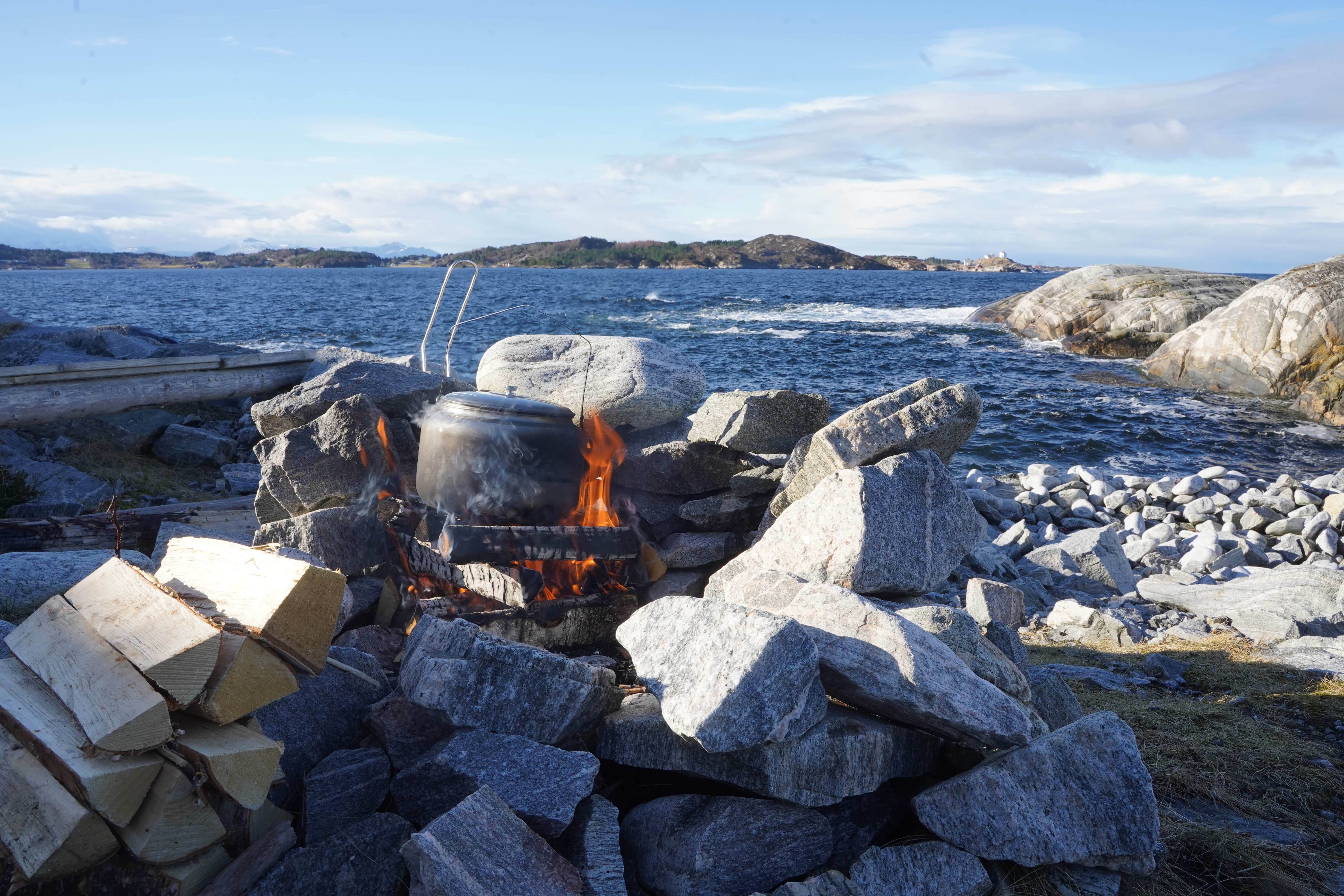 Bål i bålgrop med en kjele stående oppå Hav og Averøya i bakgrunnen