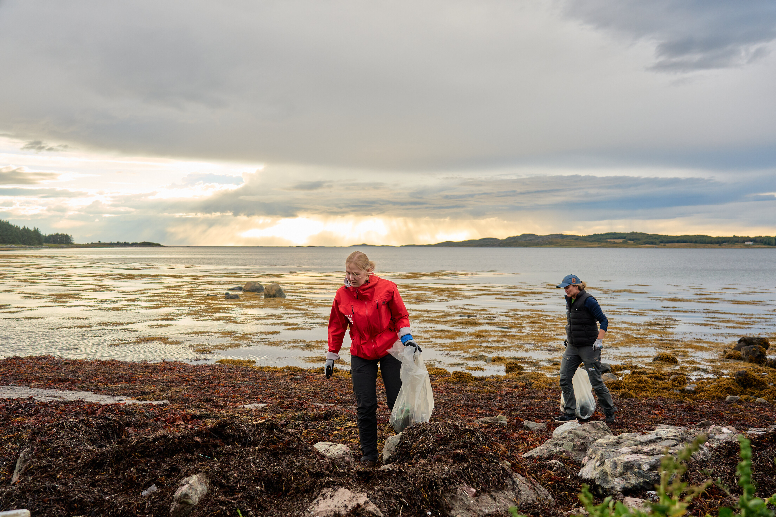 To personen rydder søppel på en strand på Smøla.