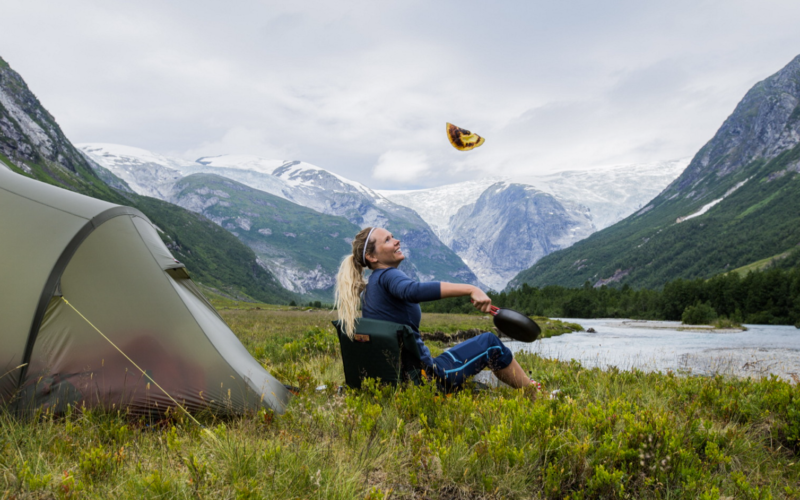 Dame sitter utenfor et telt i fjellet og flipper en pannekake.