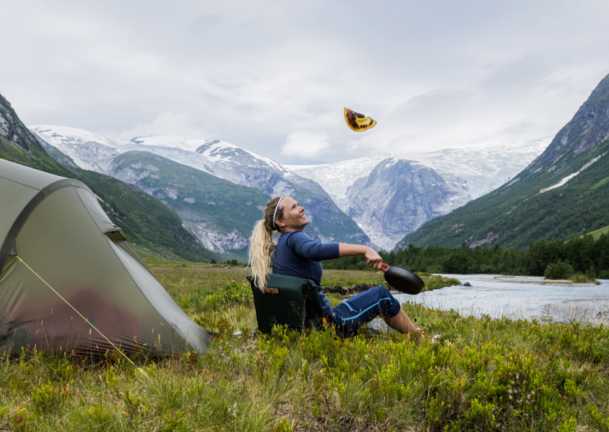 Dame sitter utenfor et telt i fjellet og flipper en pannekake.