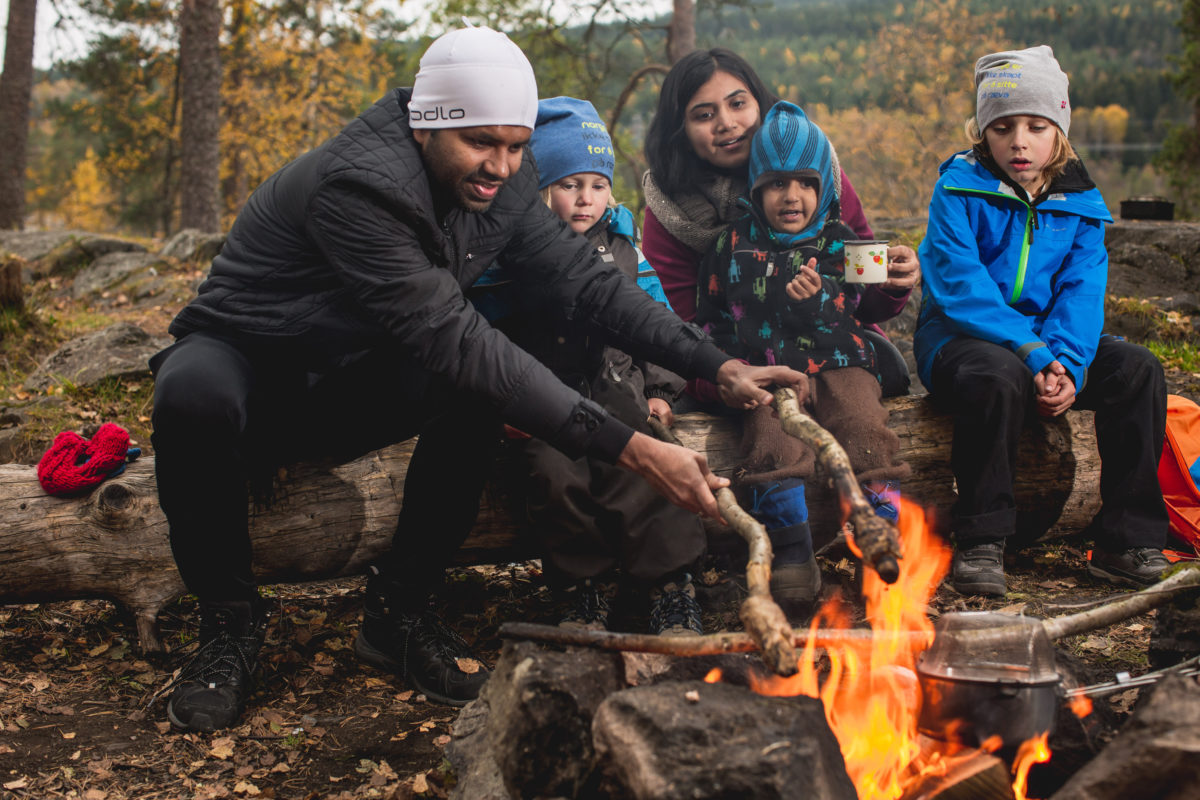 Two adults and three kids preparing food over fire, at a campsite.