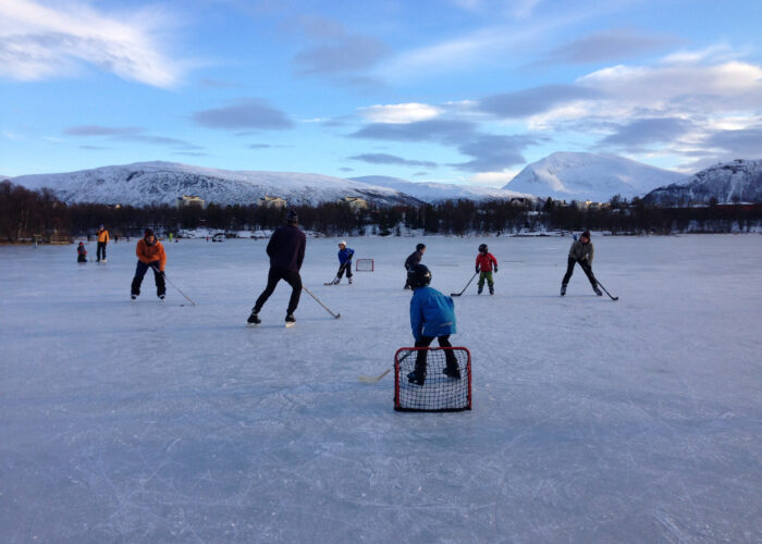 Barn og voksne spiller ishockey ute på et vann